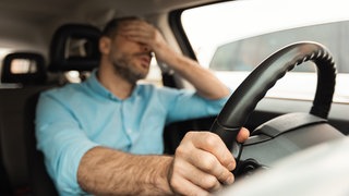 Mann am Steuer hält sich genervt die Hand vor die Augen. Wer geblitzt wird erhält Punkte in Flensburg - bis zum Fahrverbot. Bei Punktehändlern kann man sich von der Strafe freikaufen.