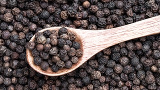 Holzlöffel liegt in schwarzen Pfefferkörnern. Pfeffer im Test: Welcher schmeckt am besten?