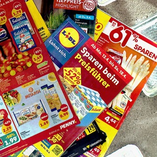 Ein Stapel Prospekte mit Angeboten: Studien belegen, es gibt weniger Sonderangebote bei Supermärkten und Discountern. Trotzdem können Verbraucher beim Einkauf von Lebensmitteln sparen.