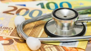 Zu sehen ist ein Symbolbild mit Geldscheinen und einem Stethoskop zum Thema Gesundheitsreform und gesetzliche Krankenversicherung