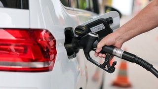 Zu sehen ist die Hand einer Person, die an einem Auto steht und tankt.