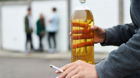 Eine jugendliche Person, sitzt auf einer Bank und raucht und trinkt Alkohol. Heute leiden Jugendliche dagegen öfter unter Depression und psychischen Problemen.