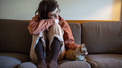 Eine junge Frau sitzt in trauriger Haltung auf einer Couch. Besonders weibliche Jugendliche sind heute von Depression und psychischen Problemen betroffen.
