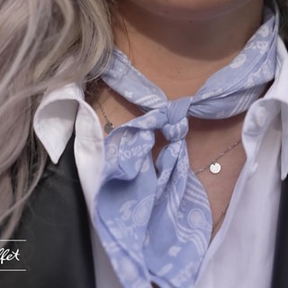 Blonde Frau trägt zu ihrem Outfit ein hellblau-weißes Halstuch