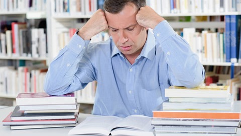 Ein Mann blickt Haare raufend und besorgt auf seinen Schreibtisch. Noch ist unklar, ob Perfektionismus bei jungen Erwachsenen und Studierenden tatsächlich Auslöser von Depressionen und Angststörungen unter jungen Erwachsenen ist - zu viele andere Einflussfaktoren könnten eine Rolle spielen.