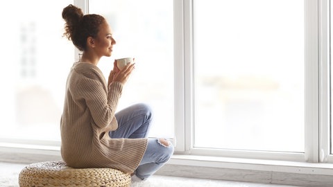Frau schaut aus dem Fenster und trinkt eine Tasse Tee