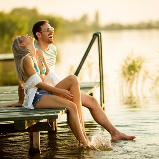 Paar sitzt entspannt auf einem Steg uns lässte die Beine ins Wasser baumeln