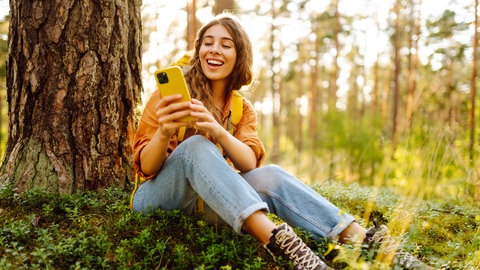 Frau sitzt mit Handy im Wald