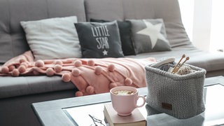 Couch mit Kissen und Häkelkorb mit Wolle auf dem Tisch