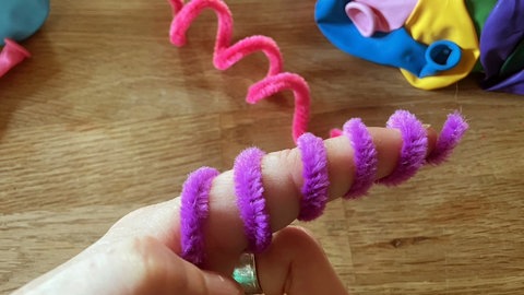 Ist der Kranz mit Luftballons bedeckt, die Pfeifenputzer um einen Finger zur Spirale wickeln und vorsichtig wieder abnehmen. Die wackeligen Spiralen unter einzelnen Luftballons durchschieben und feststecken. 