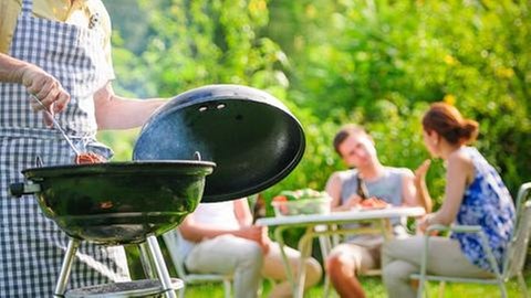 Eine Familie grillt im Grünen bei Sonnenschein.
