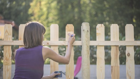 Frau streicht Gartenzaun