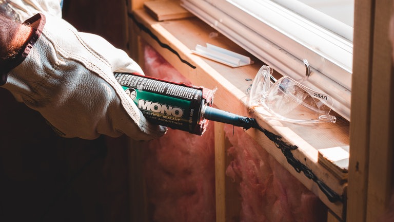 Eine Person schmiert mit einer Tube ein Fenster um es zu dämmen