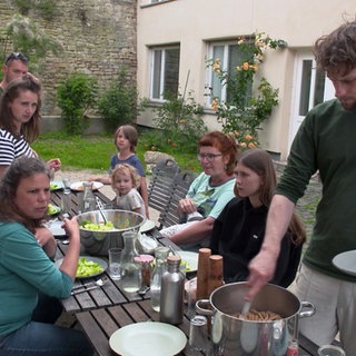Menschen im Wohnprojekt Weiselhof sitzen draußen um einen Esstisch herum