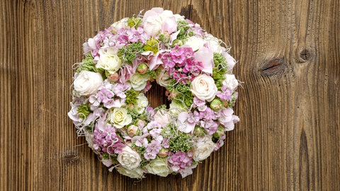 Ein Blumenkranz als Deko gesteckt aus Rosen und Nelken in Weiß und Rosa zum Frühling.