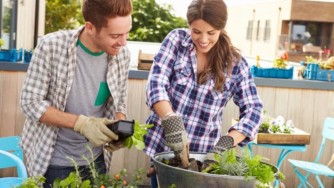 Ein Mann und eine Frau stehen auf einem Balkon. Die beiden sind dabei ganz einfach Gemüse auf ihrem Balkon anzubauen.