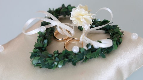 Trauringe auf einem Kissen dekoriert mit einem grünen Herz.