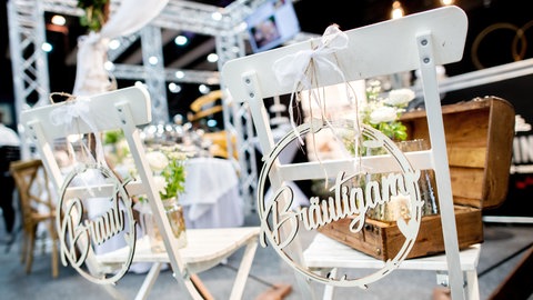 Zwei Stühle für eine Hochzeitsfeier sind mit Anhängern "Braut und Bräutigam" dekoriert. 