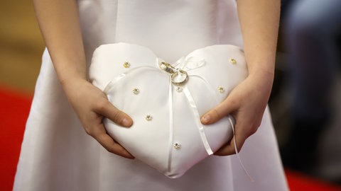 Hochzeitsringe werden auf einem Kissen in Herzform präsentiert.