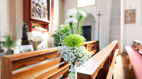 Hochzeitsdeko: Blumenschmuck an einer Kirchenbank.