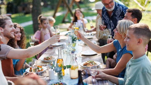 Gäste stoßen währent einer Party im Garten mit Sekt an, im Hintergrund weht eine Wimpelkette