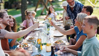 Gäste stoßen währent einer Party im Garten mit Sekt an, im Hintergrund weht eine Wimpelkette