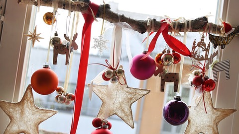 Weihnachtsdeko hängt an einem Ast im Fenster.