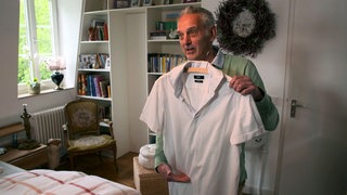 Albrecht Lang zeigt seinen Kleiderschrank und hält ein Hemd in der Hand