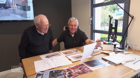 Zwei Küchenbauer sitzen am Schreibtisch und sehen sich Konstruktionspläne an