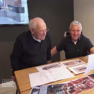 Zwei Küchenbauer sitzen am Schreibtisch und sehen sich Konstruktionspläne an