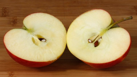 Ein Apfel liegt auf einer braunen Tischplatte in zwei Hälften aufgeschnitten da. Man erkennt die braunen Kerne.