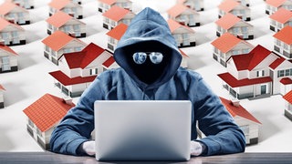 Symbolbild für Internetbetrüger bei Wohungsanzeigen: Eine vermummte, dunkle Gestalt mit Spiegelbrille sitzt vor einem Laptop. Im Hintergrund eine computergenerierte Landschaft mit Häusern.