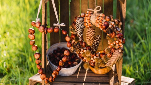 Herbstliche dekoration mit einem Kastanienherz und einem Kranz aus Kastanien, Haselnüssen und Tannenzapfen.