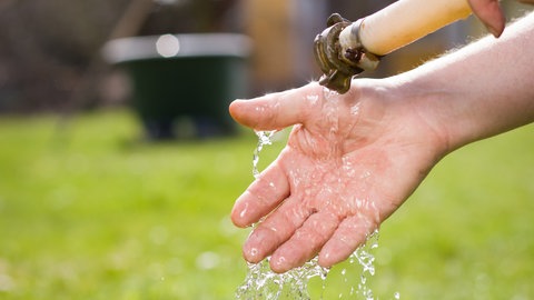 Eine Hand fängt Wasser auf, dass aus einem gelben Schlauch geflossen kommt.