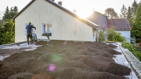 Ein Dach wird für die Dachbegrünung vorbereitet. Ein Arbeiter mit Schubkarren verteilt Dachsubstrat, in das später die Pflanzen gesetzt werden.