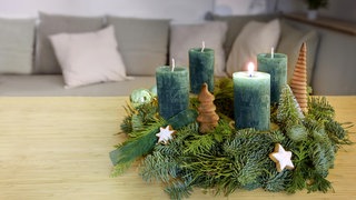 Ein Adventskranz mit grünen Tannenzweigen und türkisgrünen Kerzen.