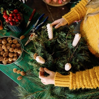Eine junge Frau dekoriert einen Adventskranz mit Kerzen und kleinen Zapfen.