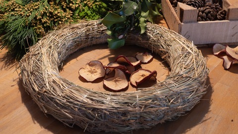Nachhaltigen Adventskranz basteln: Ein Kranzrohling, Kienäpfel und Tannengrün liegen auf einem Tisch. 
