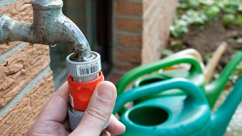 Garten winterfest machen: Ein Mann dreht im Herbst einen Gartenschlauch vom Wasserhahn ab. 