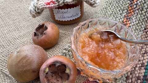 Mispelmarmelade und die Früchte der Mispel frisch aus dem Garten auf einem Tisch. Es gibt verschiedene Sorten der Mispel.
