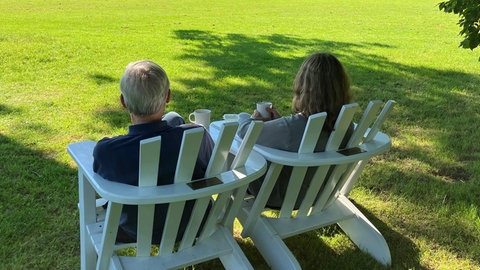 Ein Mann und eine Frau sitzen unter einem Schirmbaum und genießen im Schatten den Garten im Sommer.