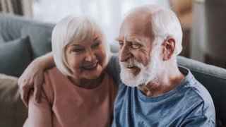 Älteres Paar sitzt auf dem Sofa und umarmt sich