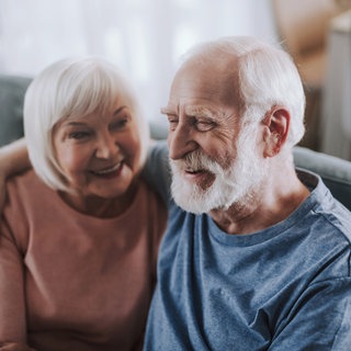 Älteres Paar sitzt auf dem Sofa und umarmt sich
