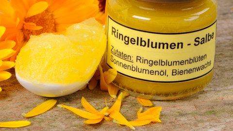 Ringelblumensalbe in einem Glas und die Blütenblätter der Ringelblume.