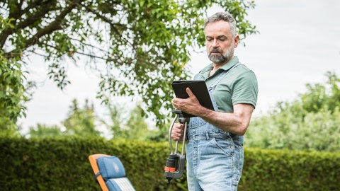 Arbeit im Garten mit einem Tablet und Rasensprenger.
