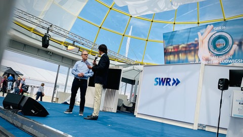 SWR-Intendant Kai Gniffke (l.) zu Besuch im Gläsernen Studio auf dem Maimarkt in Mannheim bei Moderator Leon Vucemilovic.