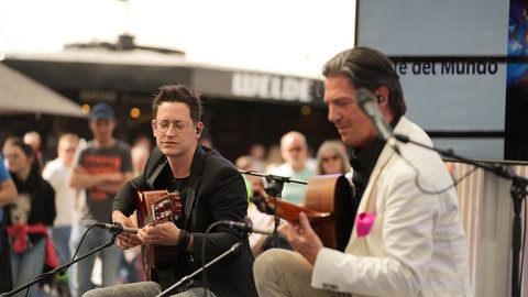 Zwei Musiker sitzen auf der Bühne und spielen Gitarre.