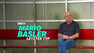 Mario Basler sitzt auf einer Bank und blickt kritisch. Darunter steht der Schriftzug: MARIO BASLER - Letzter Typ.