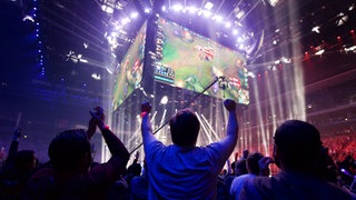 Zuschauer jubeln bei einem Livestream von League of Legends auf einer großen Leinwand.