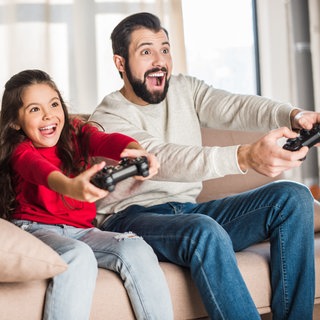 Ein Vater und seine Tochter sitzen auf der Couch und zocken gemeinsam.